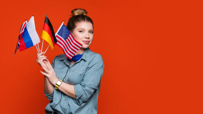 Caucasian student girl holds set small flags. Study abroad concept. International student exchange program. Female student recommending foreign language studying school. Copy Space