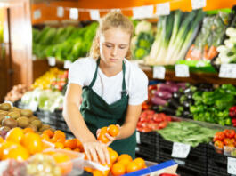 Cheerful young girl employees in uniform holding fresh mandarines in grocery shop