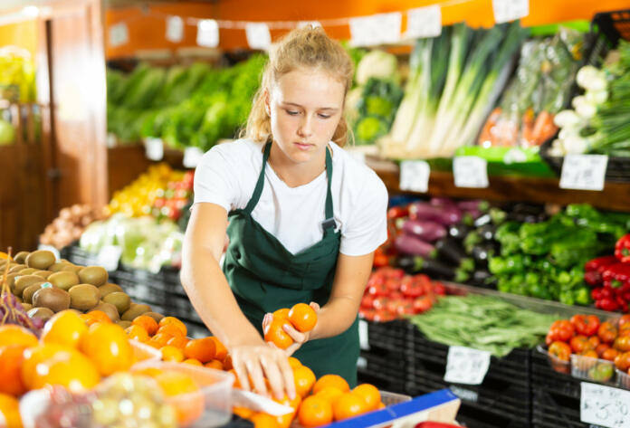 Cheerful young girl employees in uniform holding fresh mandarines in grocery shop