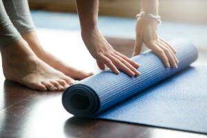 Close-up of attractive young woman folding blue yoga or fitness mat after working out at home in living room. Healthy life, keep fit concepts. Horizontal shot