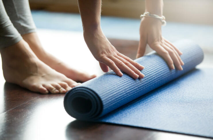 Close-up of attractive young woman folding blue yoga or fitness mat after working out at home in living room. Healthy life, keep fit concepts. Horizontal shot