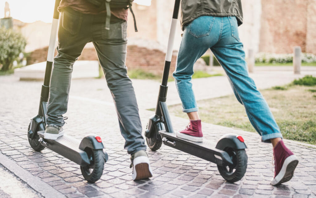 Close up of people couple using electric scooter in city park - Millenial students riding new modern ecological mean of transport - Green eco energy concept with zero emission - Warm sunshine filter