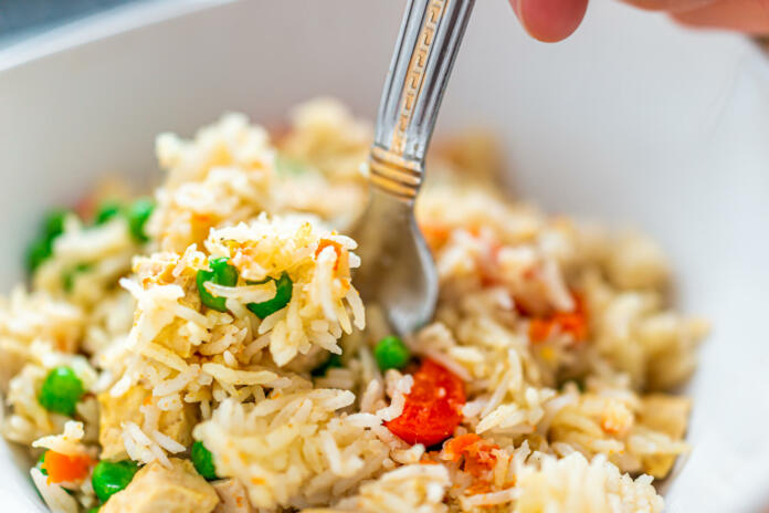 Closeup macro of fresh colorful basmati rice dish with green peas, curry and carrots with tofu and hand holding fork in bowl