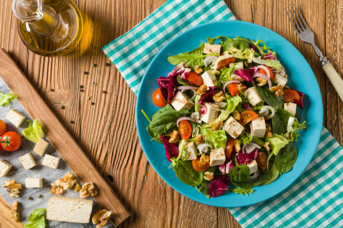 Delicious salad with tofu, tomatoes and walnuts, drizzled with a sauce of balsamic vinegar and served on a blue plate. Top view.