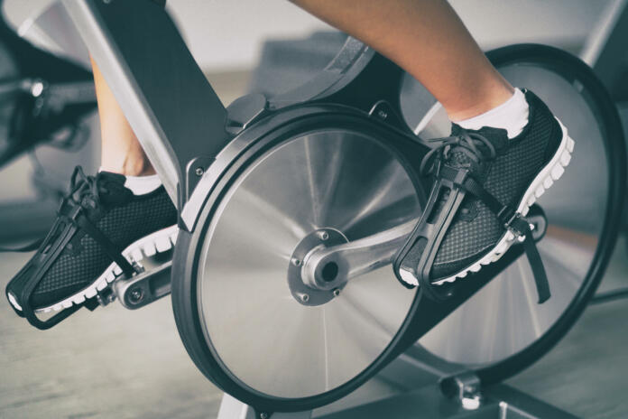 Fitness machine at home woman biking on indoor stationary bike exercise indoors for cardio workout. Closeup of shoes on bicycle.