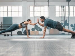 Fitness partners exercising together and doing pushups high five at the gym. Fit and active man and woman training in a health facility as part of their workout routine. A couple doing an exercise