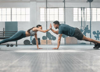 Kako začeti bolj redno trenirati? Fitness partners exercising together and doing pushups high five at the gym. Fit and active man and woman training in a health facility as part of their workout routine. A couple doing an exercise