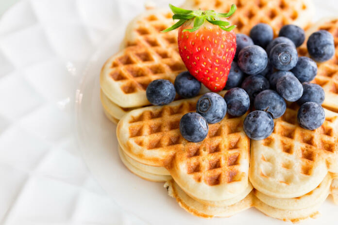 Fresh homemade heart shape waffles with blueberries and strawberry on white plate