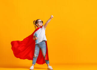 5 navdihujočih filmov za študente v izpitnem obdobju Full body girl in superhero cape smiling and raising fist up while being ready for school studies against yellow backdrop