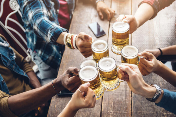 Group of people enjoying and toasting a beer in brewery pub - Friendship concept with young people having fun together