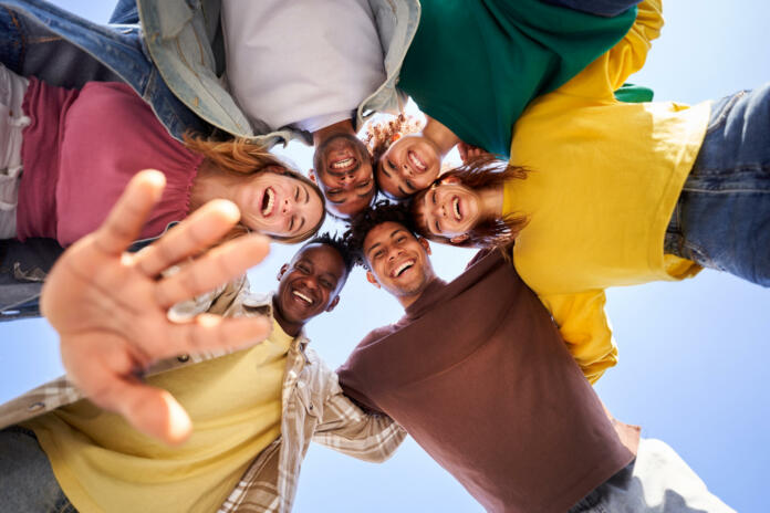 Internacional Erasmus students looking at camera cheerfully embracing each other. Group of people in circle looking down. Low angle view. Copy space.