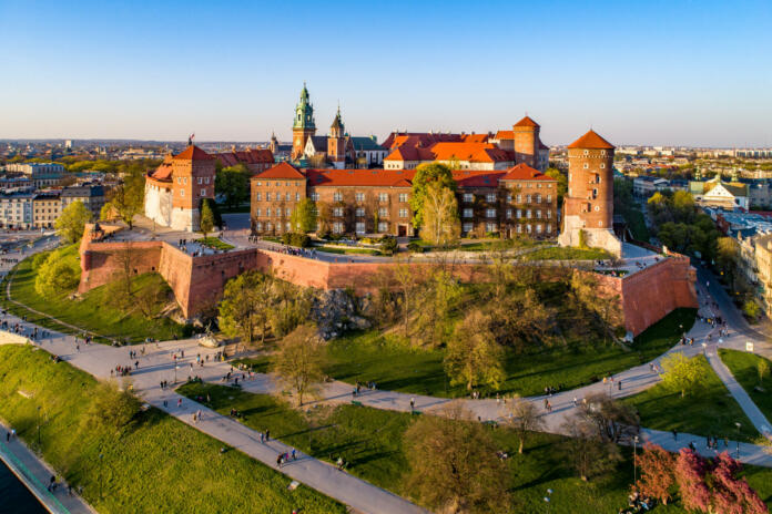 Kraków, Poland – April 04, 2019:  Skyline panorama of Cracow old city with Wawel Hill,  Cathedral, Royal Wawel Castle, defensive walls, park, promenade and unrecognizable walking people.