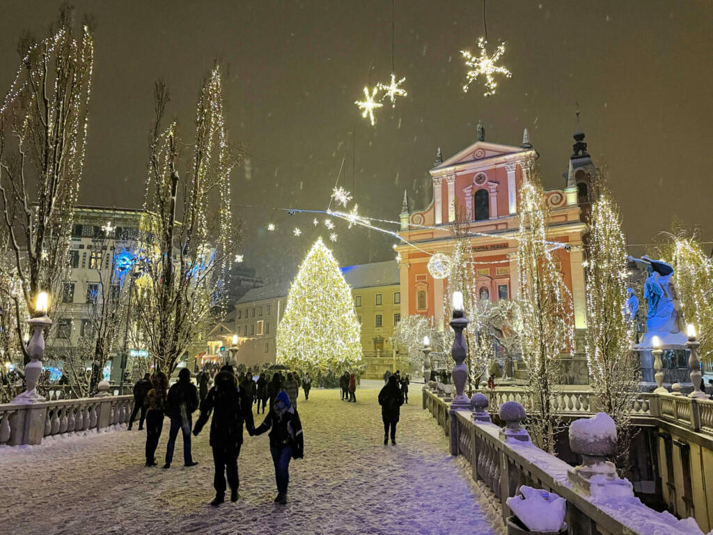 LJUBLJANA, SLOVENIA, DECEMBER 2020: Tourists walk across a bridge and towards the massive Christmas tree in the middle of Preseren square. Masses of people explore the charming streets of Ljubljana.