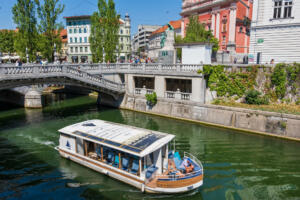Ljubljana, Slovenia - July 13, 2022: Tour boat at Triple Bridge on Ljubljanica River in the city center, sightseeing river cruise.