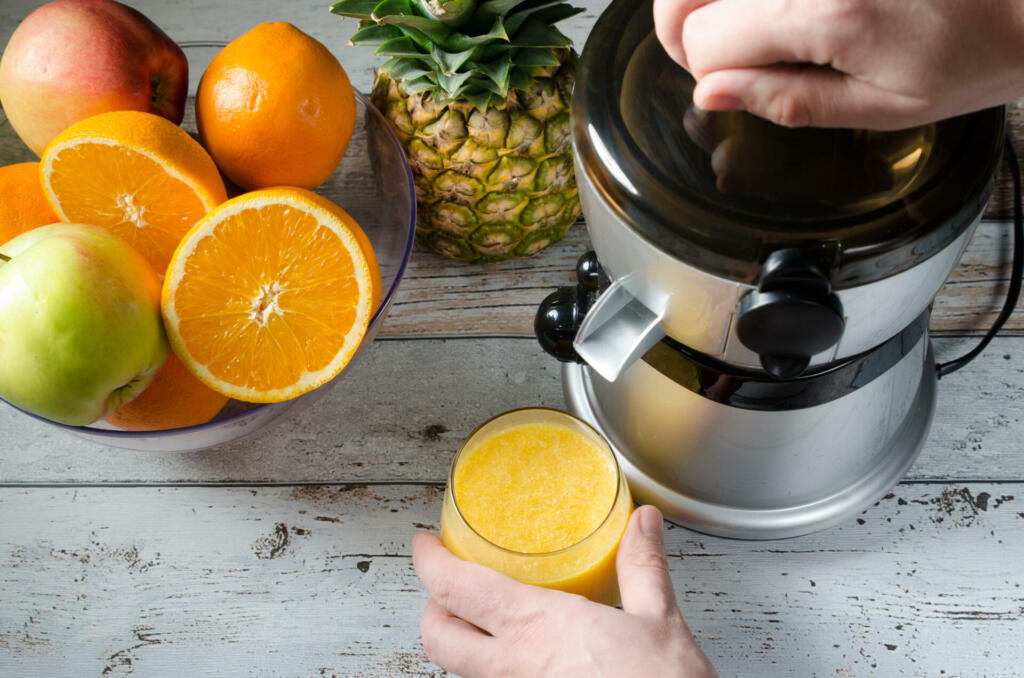 Man preparing fresh orange juice. Fruits in background on wooden desk