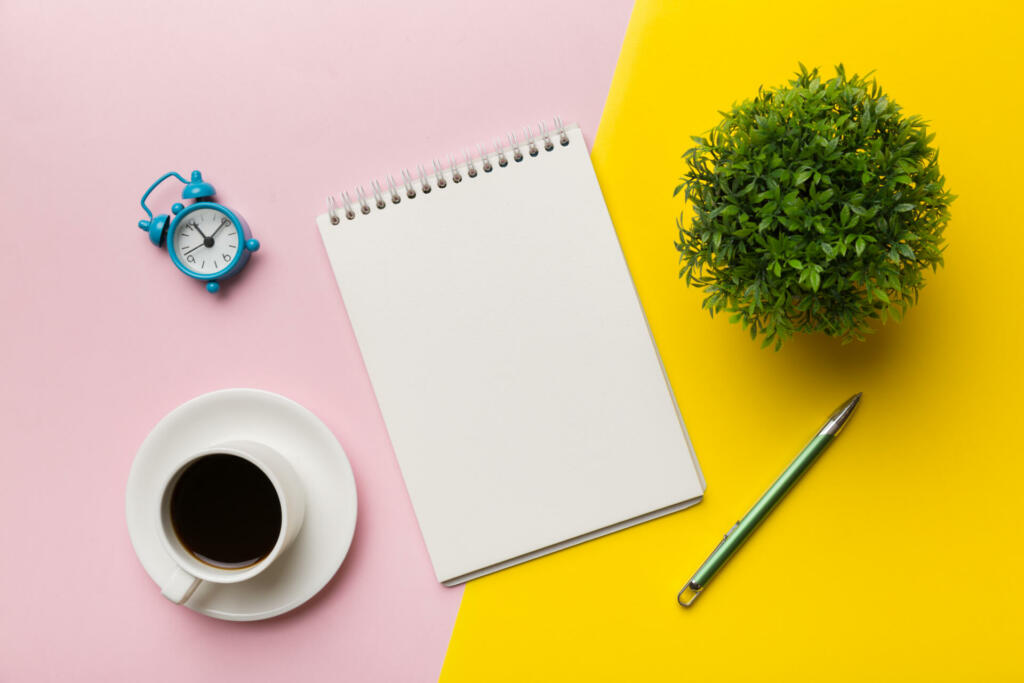 Modern office desk table with notebook and other supplies with cup of coffee. Blank notebook page for you design. Top view, flat lay.