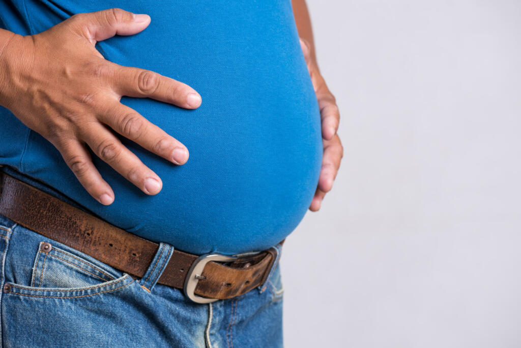 Overweight or fat adult man in very tight jeans on a gray background. Healthcare, medicine concept.