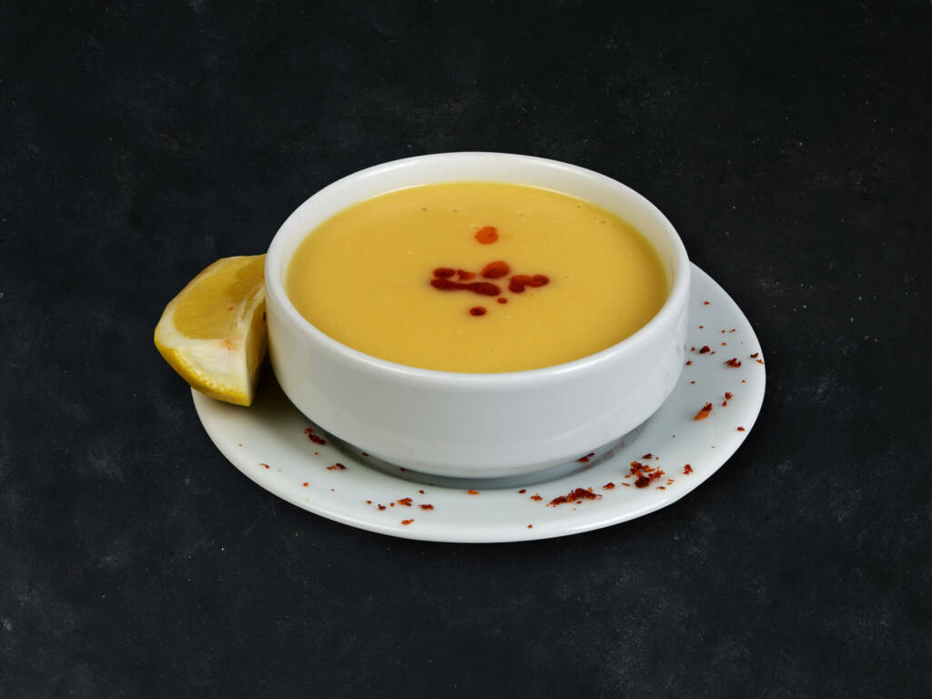 Red lentil soup in white plate on black stone background.