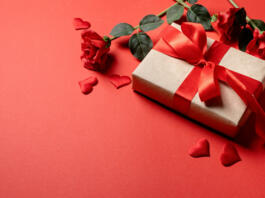 Red solid background with red hearts, gifts and confetti. The concept of Valentine Day.