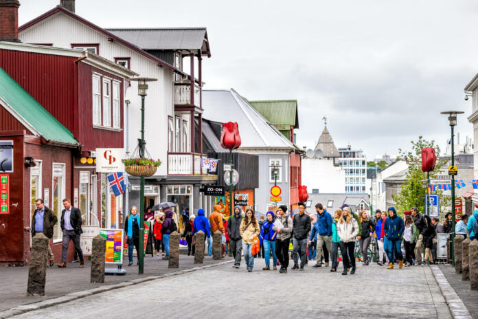 Reykjavik, Iceland - June 19, 2018: Many people tourists walking on street sidewalk in downtown center by stores shops restaurant with signs in summer
