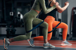 Sporty women in gym exercising with elastic resistance rubber band.