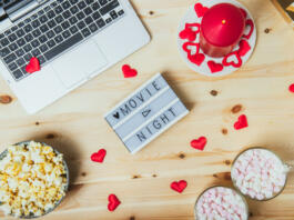 St. Valentine's day Movie night concept. Movie night message on board, laptop, popcorn, red candle, gift, hearts decor, two cups of cocoa with marshmallows for a couple. Cozy holiday plans for lovers