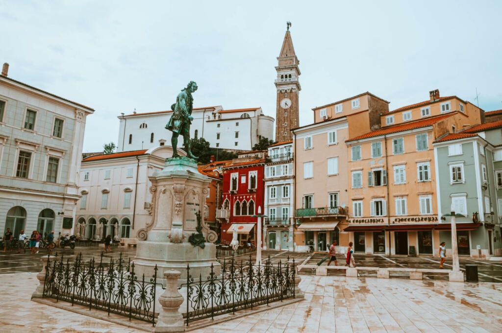 Kip na sredini trga, v okolici stare zgradbe in zvonik