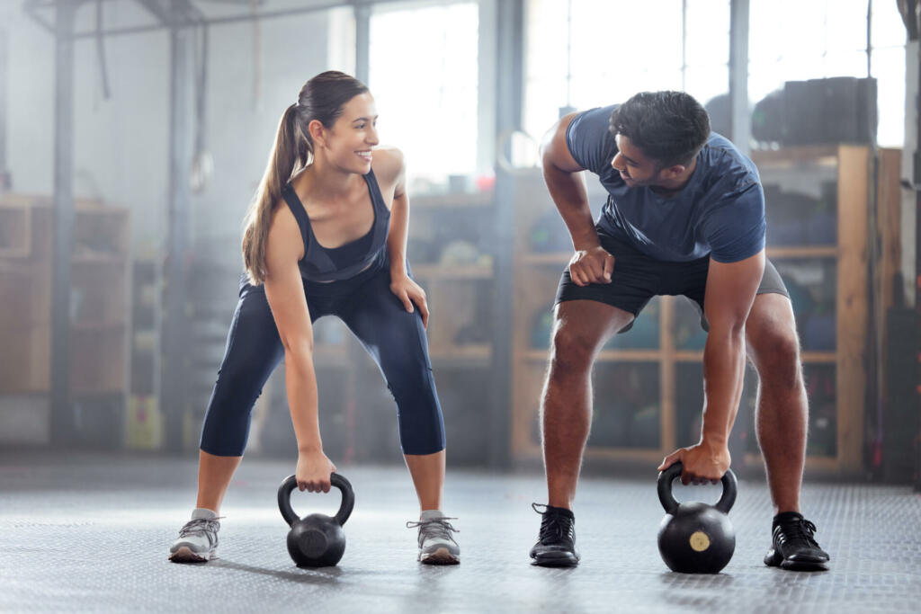 Strong, wellness couple doing kettlebell weight exercise, workout or training inside a gym. Happy sports people or trainer motivation, exercising with fitness equipment for muscle, strength or health