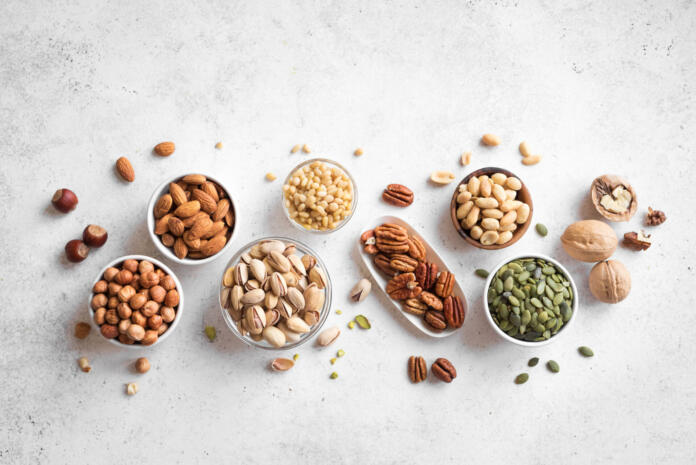 Various Nuts in  bowls on white background, top view, copy space. Nuts assortment - pecans, hazelnuts, walnuts, pistachios, almonds, pine nuts, peanuts, pumpkin seeds.