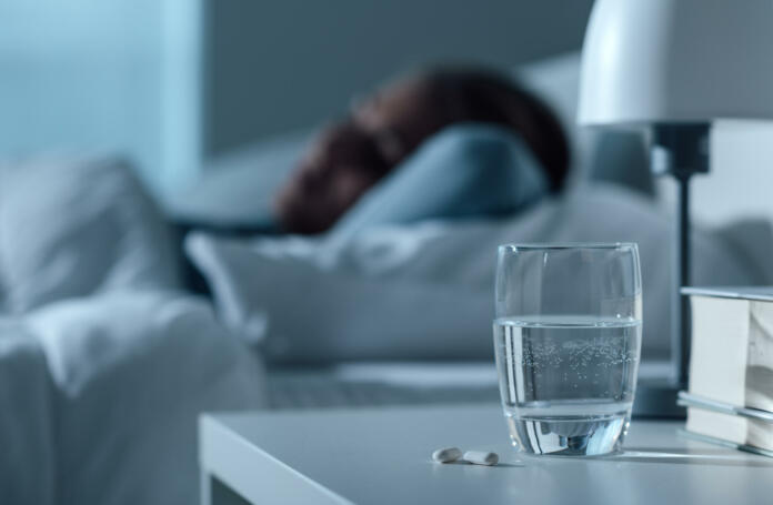 Woman sleeping in her bed at night, glass on water and pills on the foreground, medicine and treatment concept