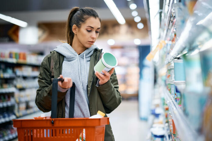 Young woman buying diary product and reading food label in grocery store.