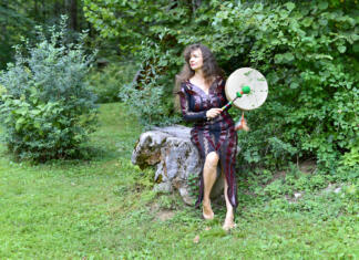 Poglobljen tečaj senzualne masaže Ženska sedi na kamnu in v rokah drži boben, v ozadju se vidi gozd