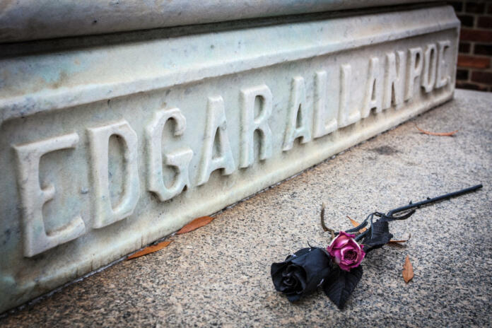 base of Poe tombstone with carved name - black and purple rose laid in front