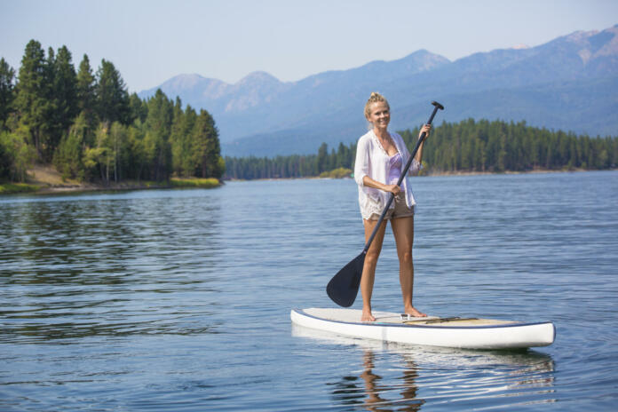 Beautiful woman paddle boarding on scenic mountain lake while enjoying an relaxing vacation. Lots of copy space