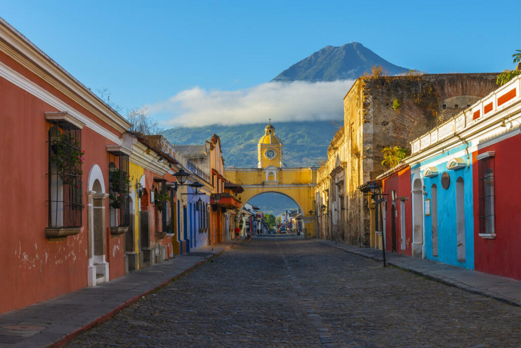 Cityscape of the main street and yellow Santa Catalina arch in the historic city center of Antigua at sunrise with the Agua volcano, Guatemala.