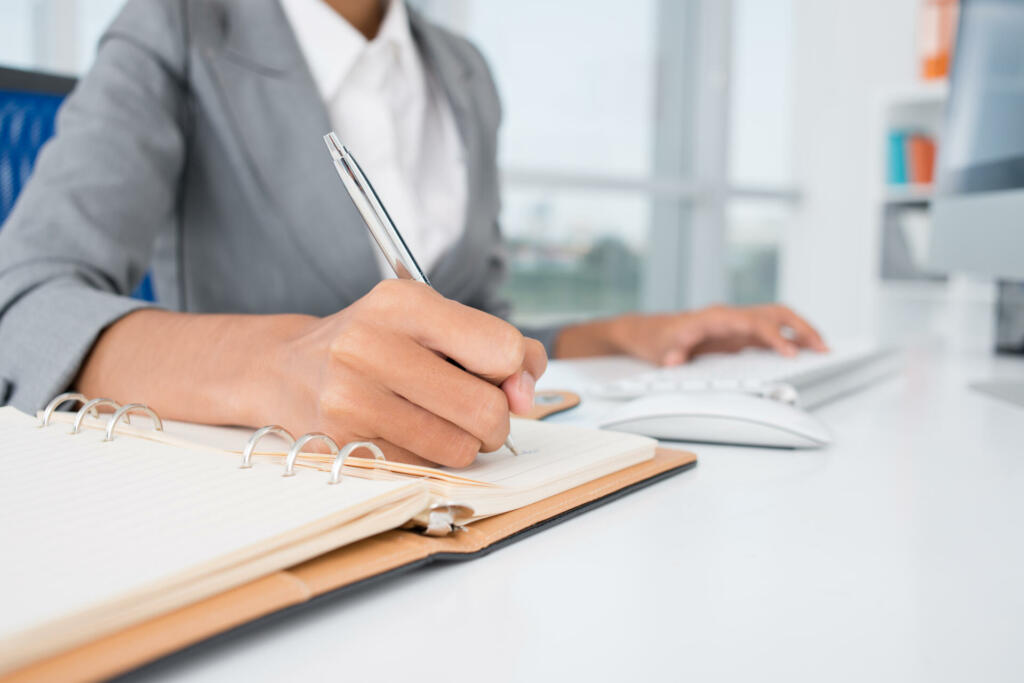 Close-up of female hands making notes in the notepad at office