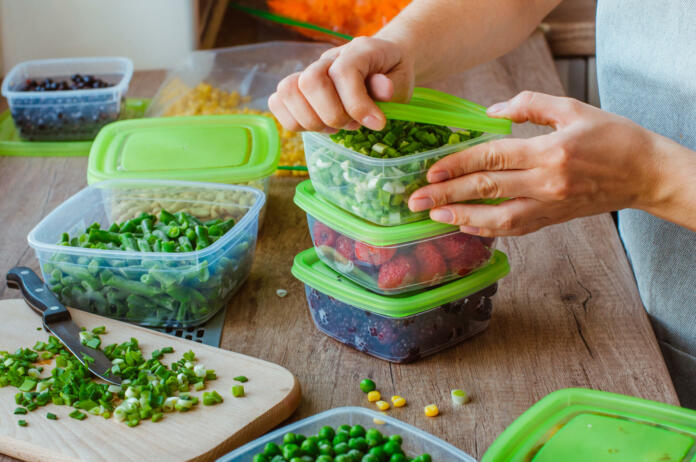 Close up of woman preparing plastic food boxes with fresh green onion, strawberry and blackberry for freezing on the wooden table.