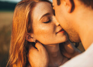 Pogrešaš partnerja? Kitajci imajo rešitev Close-up portrait of a freckled girl kissing her boyfriend while they are on an outdoor date. Wheat field. People lifestyle concept.