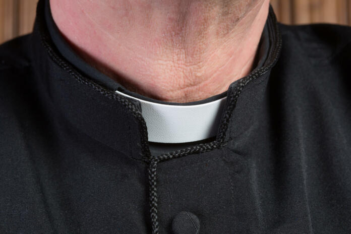 Closeup of the neck of a priest wearing a black shirt with cassock and white clerical collar