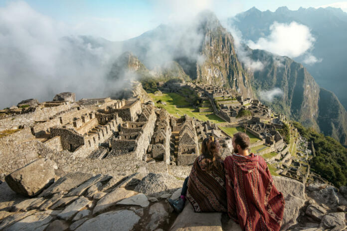 Couple dressed in ponchos watching the ruins of Machu Picchu