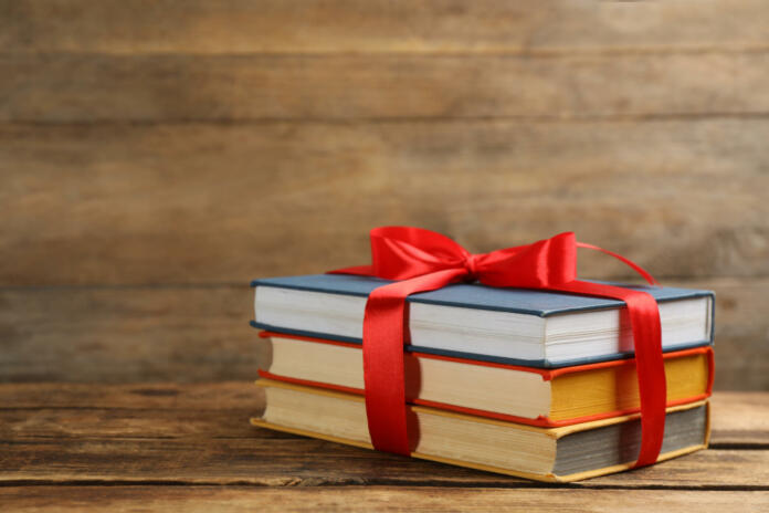 Different books tied with red ribbon on wooden table, space for text