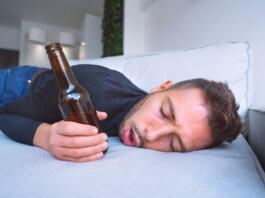 Drunk young man with open mouth and bottle of beer sleeping on the sofa at home. High quality photo
