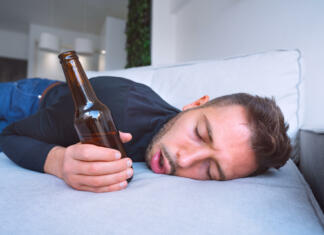 Katera država v Evropi popije največ alkohola? Drunk young man with open mouth and bottle of beer sleeping on the sofa at home. High quality photo