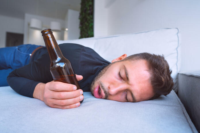 Drunk young man with open mouth and bottle of beer sleeping on the sofa at home. High quality photo