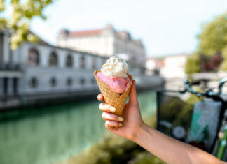 Najboljši sladoled v Ljubljani za leto 2023 Female hand holding ice cream cone on the water chanal and bicycle on the background in Ljubljana city. Slovenian street food