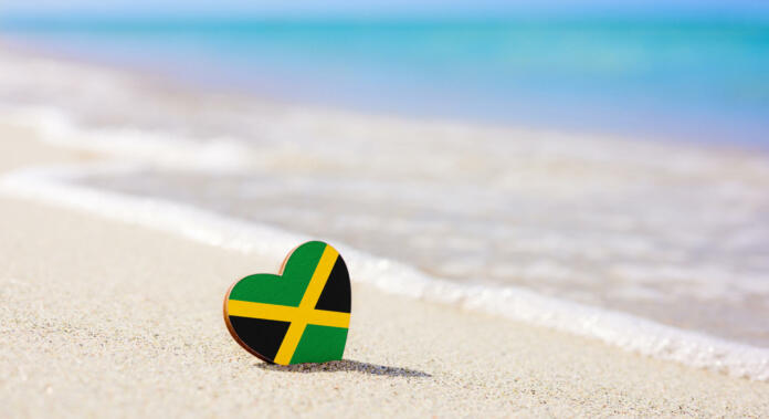 Flag of the Jamaica in the shape of a heart on a sandy beach. The concept of the best vacation in Jamaica