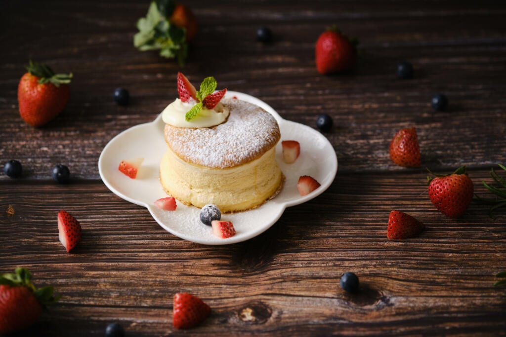 Fluffy souffle pancakes with cream and berries on white plate set on wooden table.