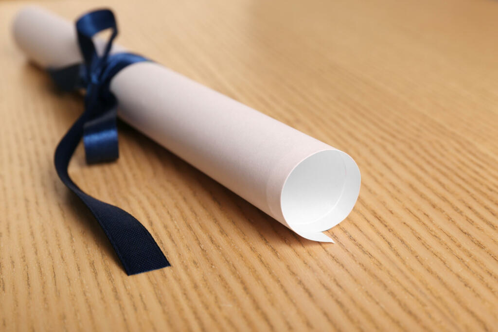 Graduation diploma tied with blue ribbon on wooden table, closeup