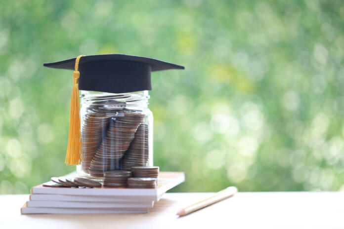 Graduation hat on coins money in the glass bottle on natural green background, Saving money for education concept