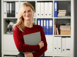 Happy smiling blond businesswoman holdig gray folder in hand office workplace look at camera